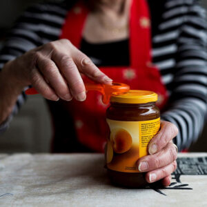 Henkilö avaa lasipurkin kantta purkinavaamista helpottavalla apuvälineellä.