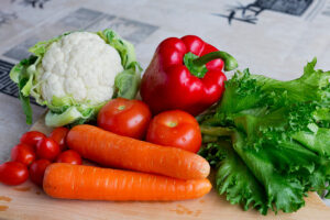 Kukkakaali, tomaatteja, porkkanoita, punainen paprika ja salaatinlehtiä leikkuulaudalla.