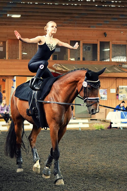 Nainen tasapainoilee hevosen selässä esiintymisasussa.
