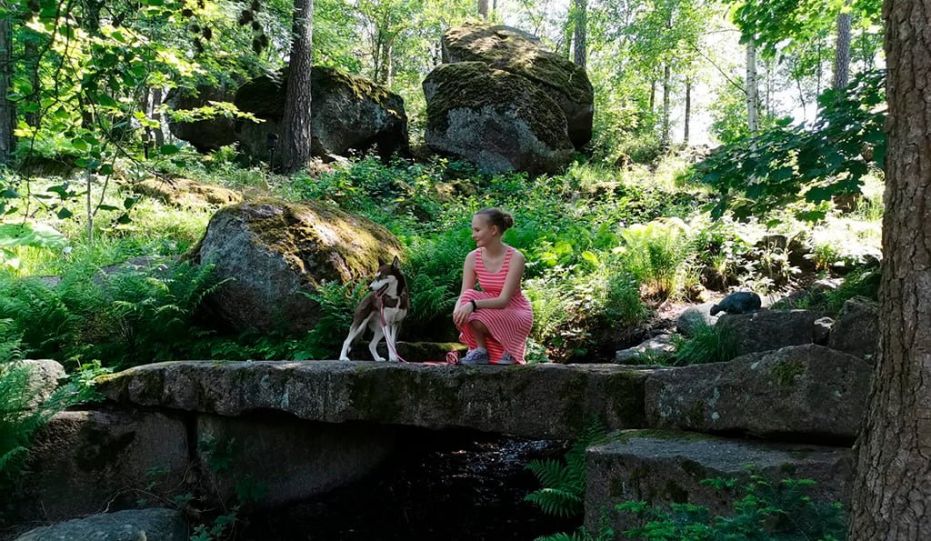 Nuori nainen ja koira kesäisessä, vihreässä maisemassa.