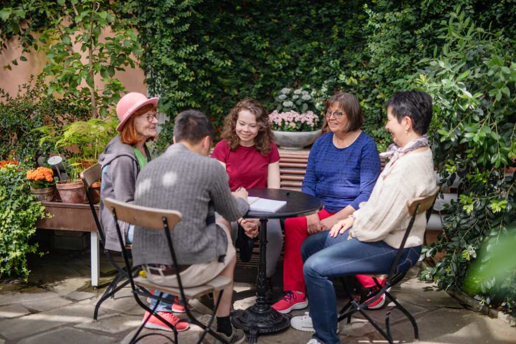 Ihmisiä puutarhassa pyöreän pöydän ympärillä iloiset ilmeet kasvoillaan.