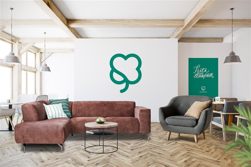Olohuone, jossa sohva ja nojatuoli sekä seinällä Reumaliiton logo.