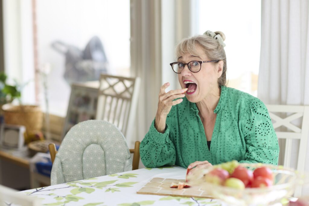 Nainen syö omenalohkoa pöydän ääressä. Naisen sorminivelet ovat muhkuraiset.
