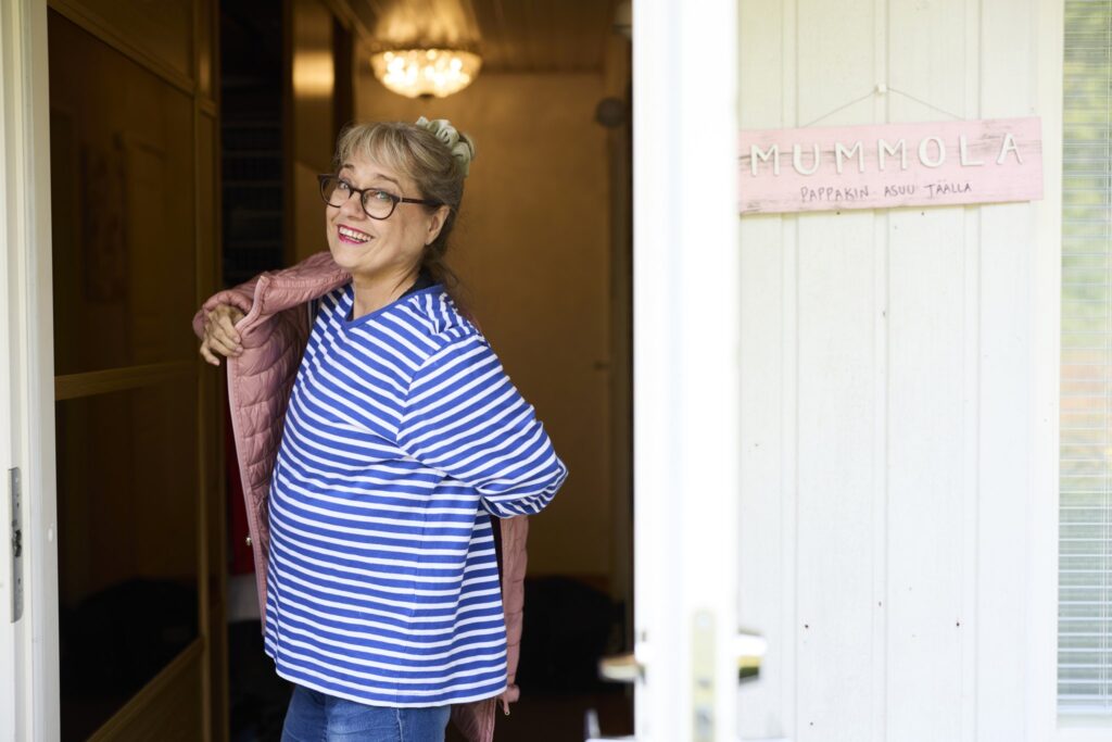 Nainen katsoo kameraan ja pukee päälle vaaleanpunaista takkia.