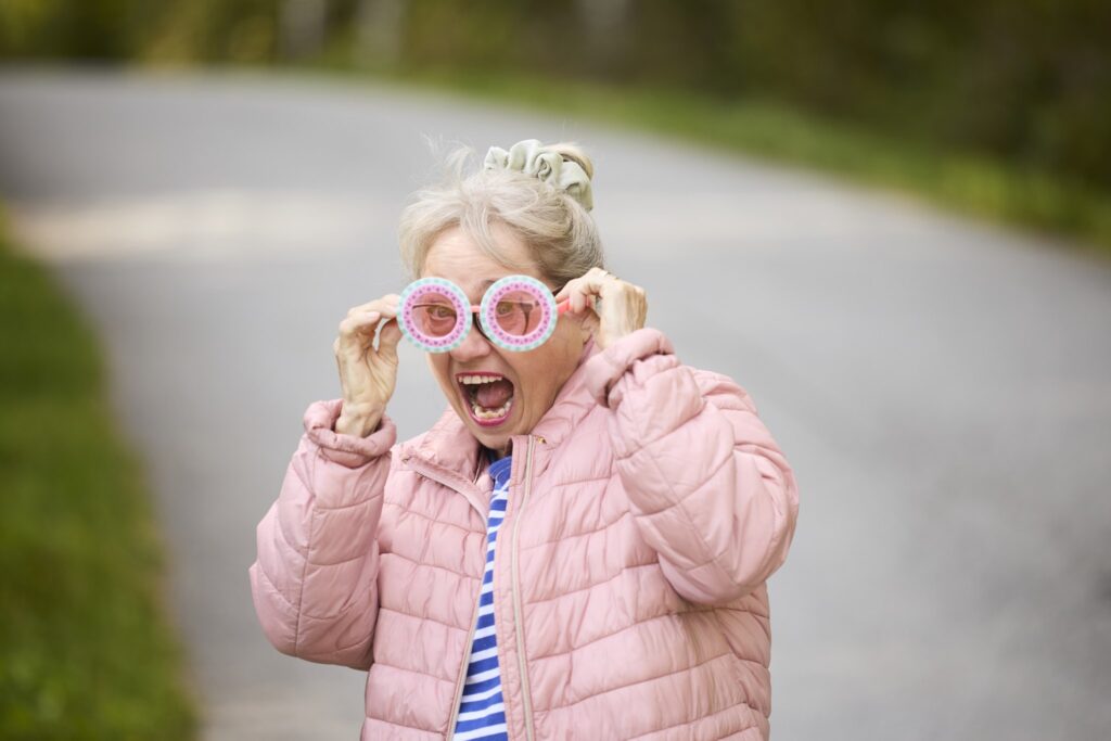 Nainen katsoo kameraan ja virnistää, silmillään hassut vaaleanpunaiset lasit.