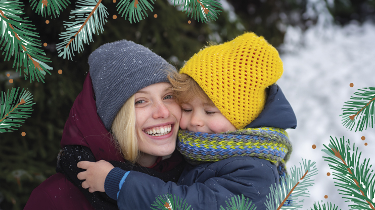 Nainen ja lapsi halaavat ulkona pipot päässä. Etualalle lisätty piirrettyjä havuja.