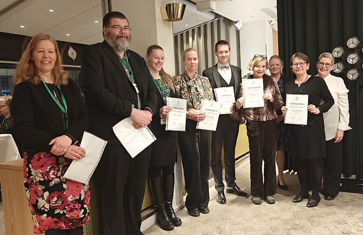 Ihmisiä seisomassa kaaressa kädessään kunniakirjat.